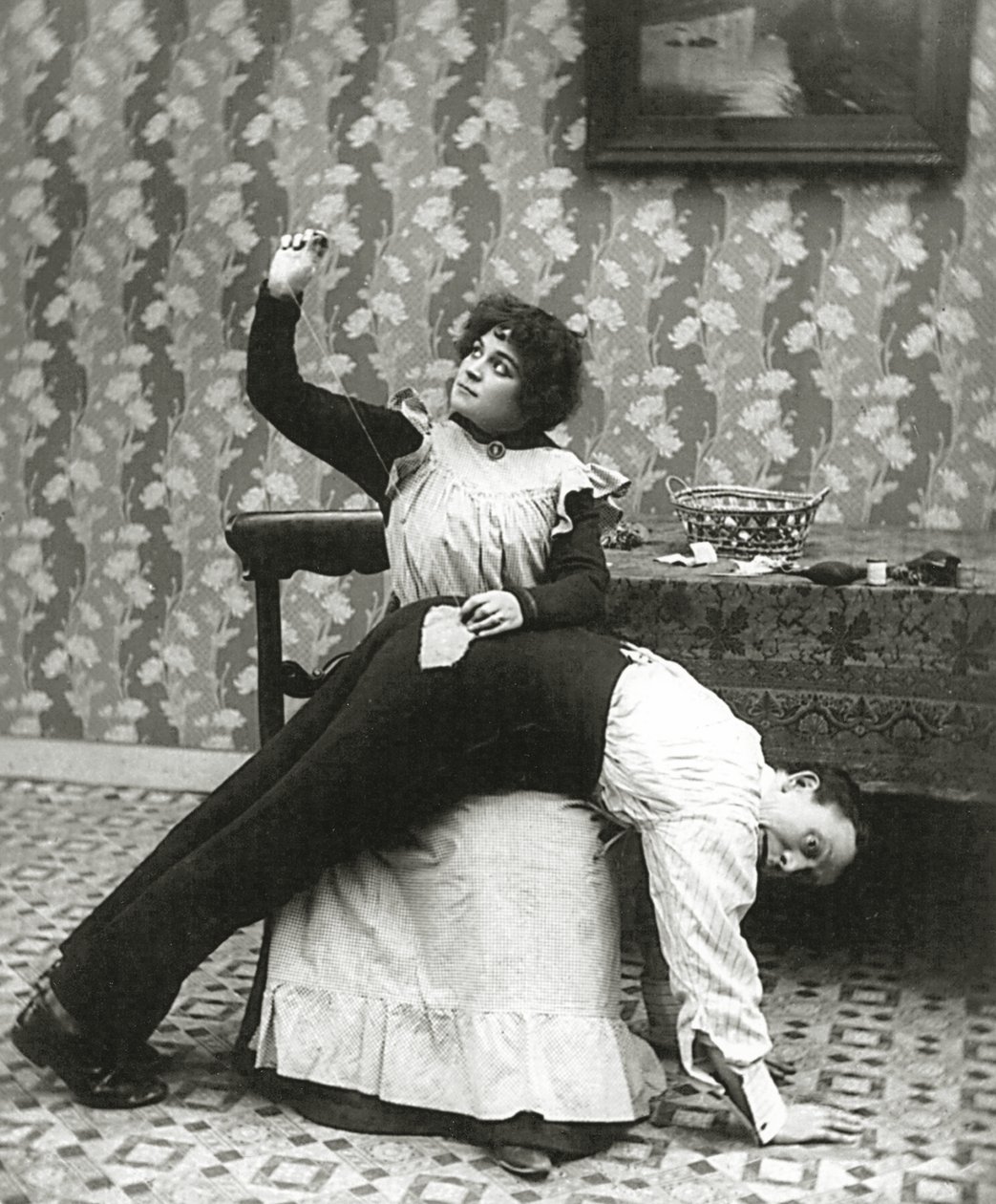 Woman sewing a tear on a mans trousers, c.1895 by American Photographer