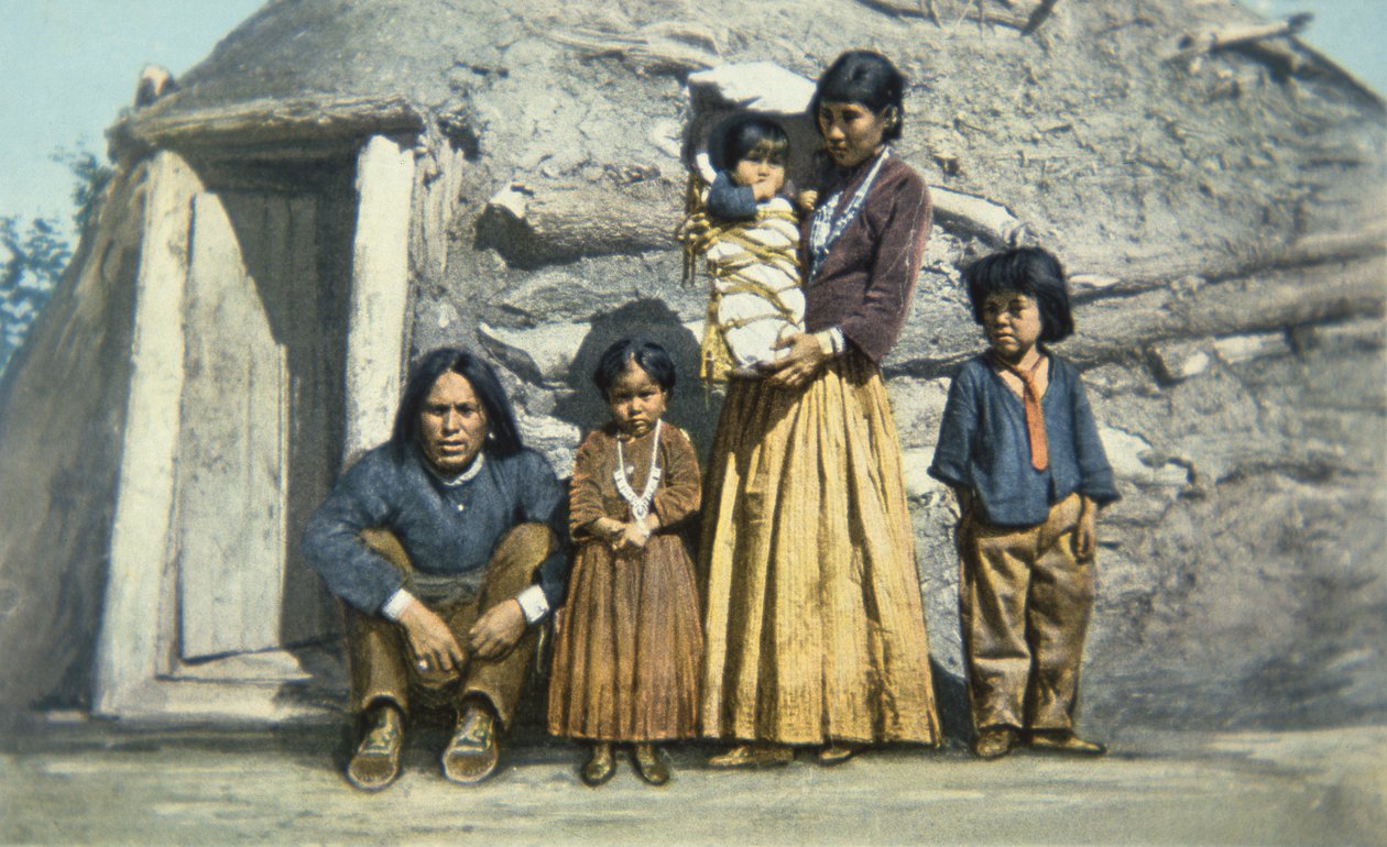 Postcard of a Navajo indian family outside their house or 