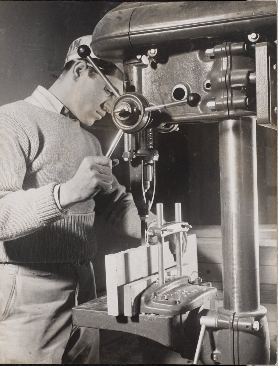 Man uses a machine to drill holes in two wood blocks by Arnold Eagle