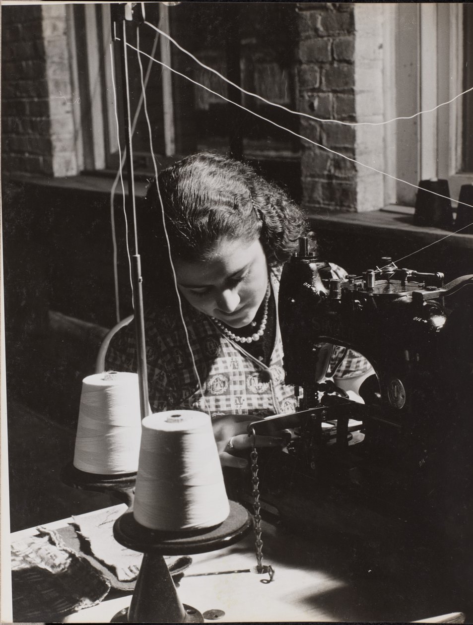Woman using a sewing machine with two spools of white thread by Arnold Eagle