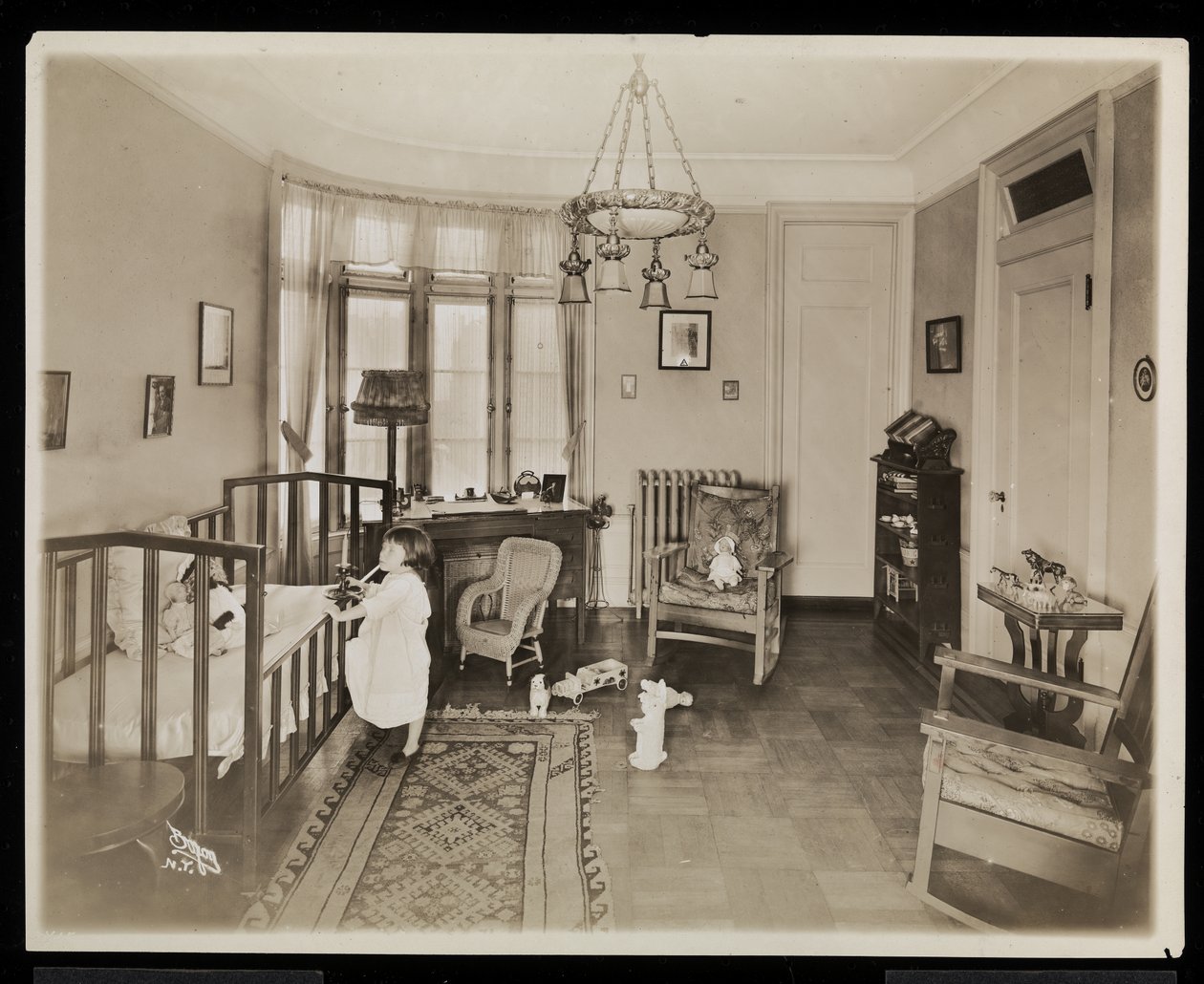 A girl holding a candle, climbing into a crib, in a bedroom of the A.C. Cronin residence by Byron Company