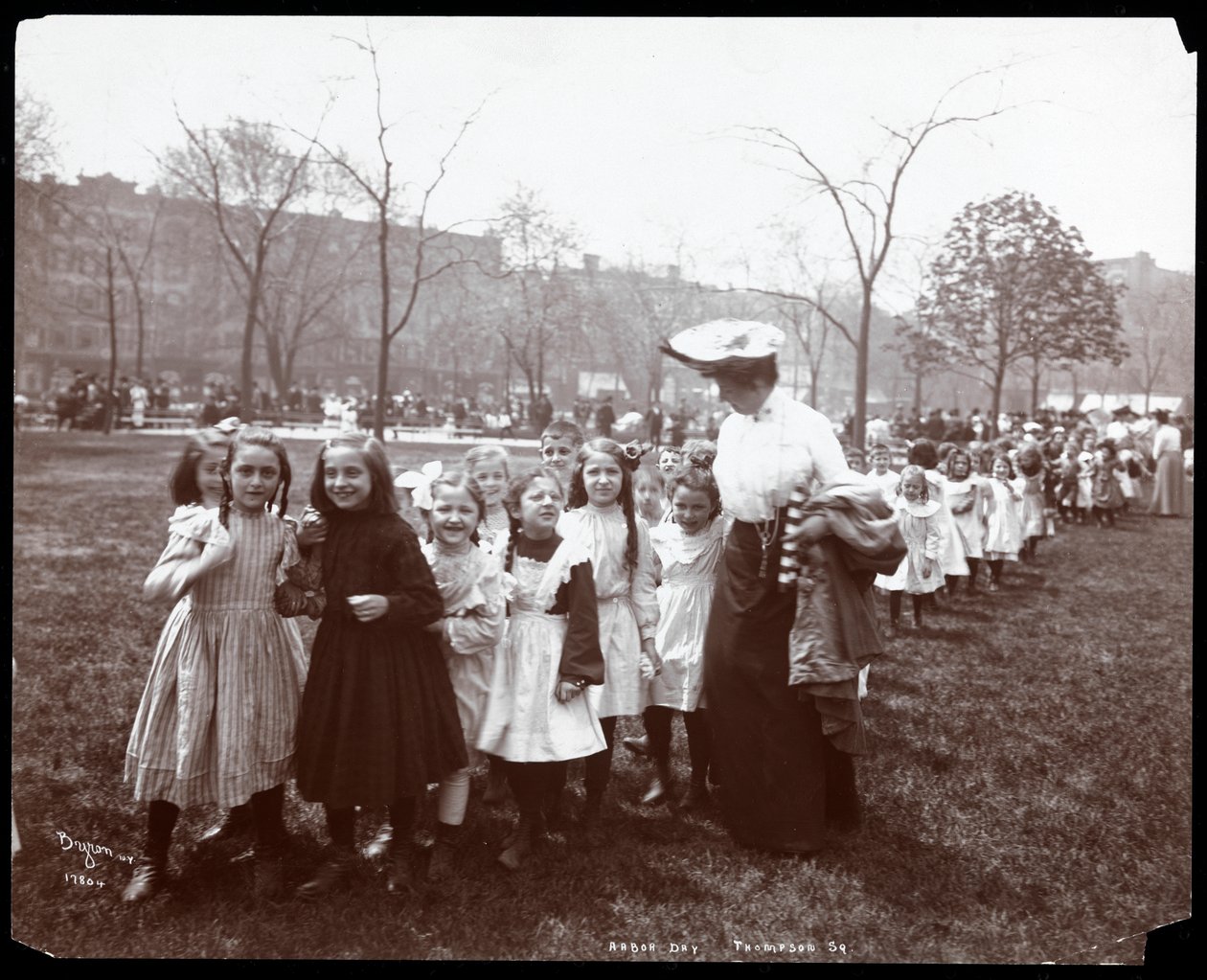 Children in a long line being led by a woman on Arbor Day at Tompkins Square Park, New York, 1904 by Byron Company