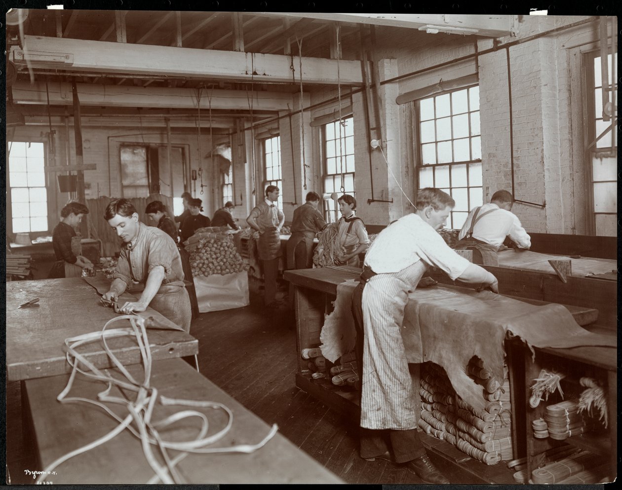 Interior view of men and women working with leather at the New York Leather Belting Co., New York by Byron Company