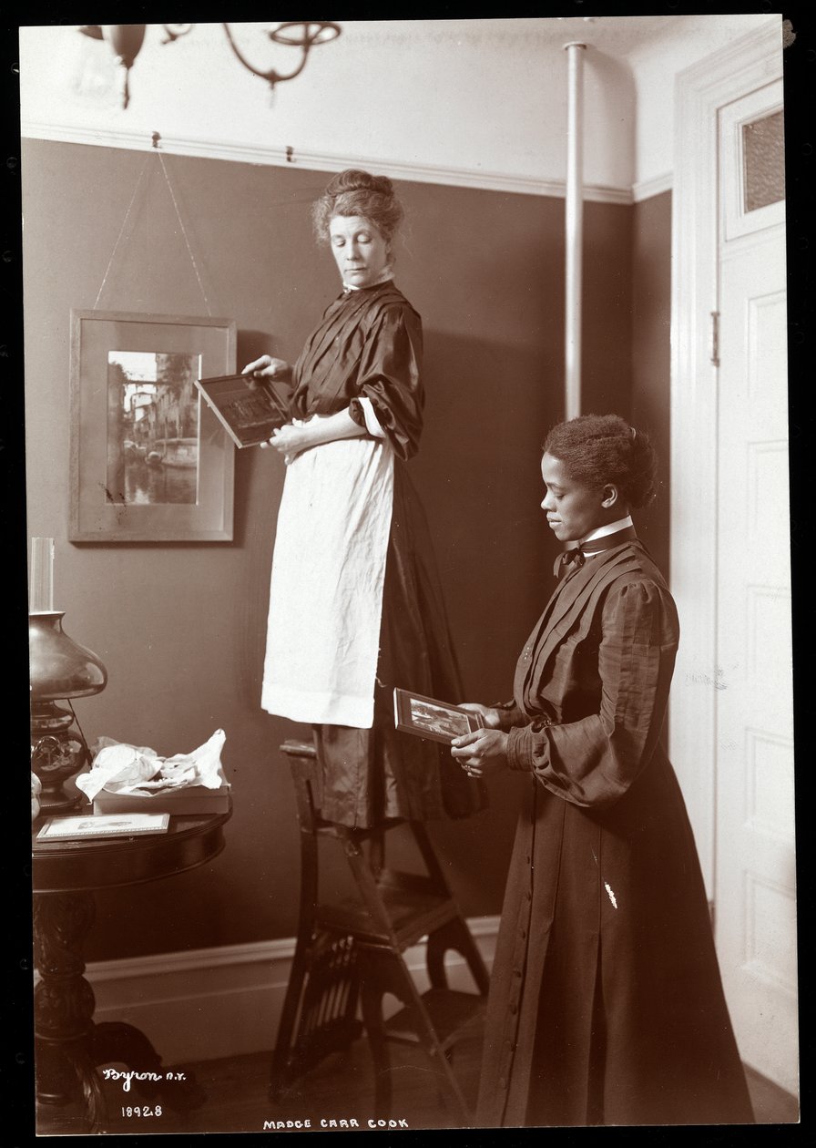 Madge Carr Cook hanging pictures with her maid by Byron Company