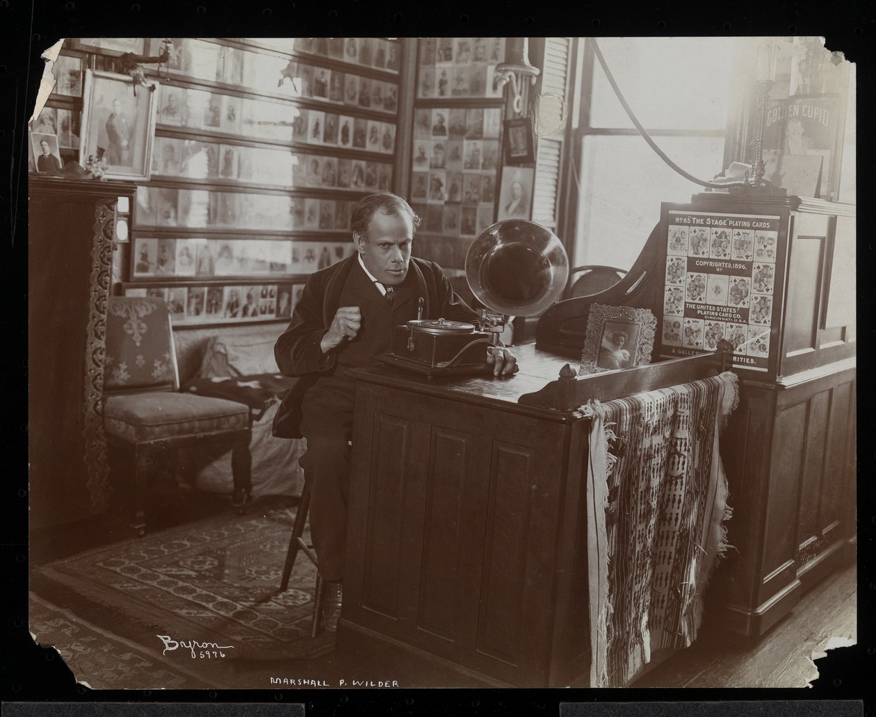 Marshall P. Wilder listening to a record on a victrola in his office by Byron Company