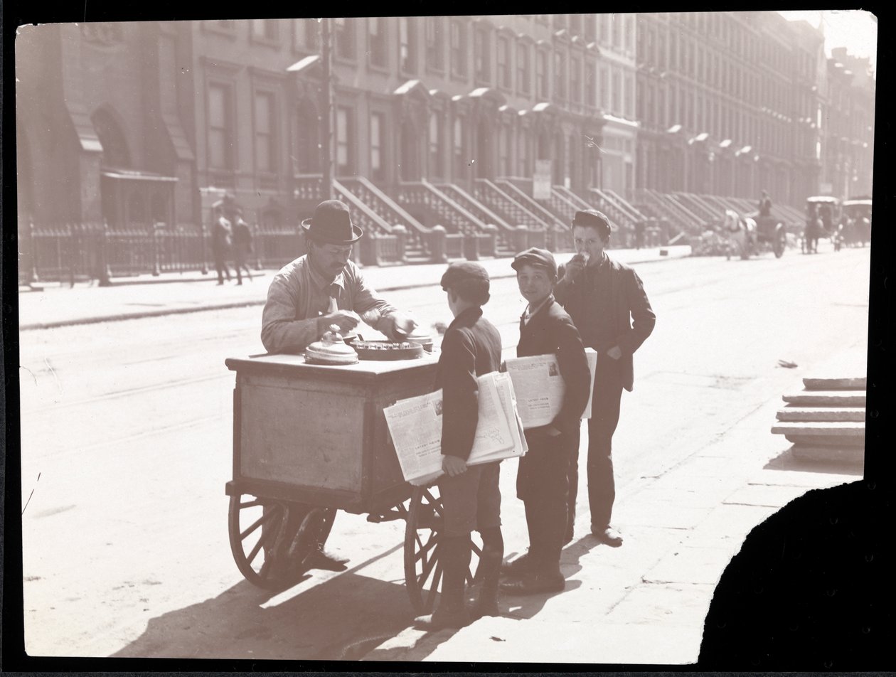 View of an ice cream peddler on the street, with three newsboys buying ice cream, New York by Byron Company