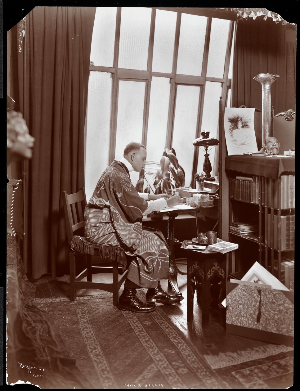 Will R. Barnes in a robe, seated at his desk in his studio, 1903 by Byron Company