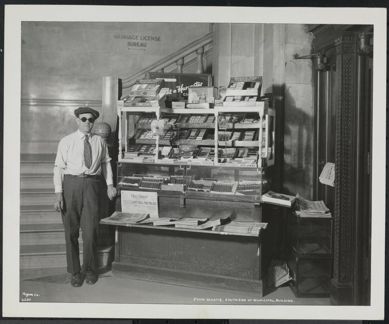 Blind news dealer, John Martie, at his stand at the south end of the Municipal Building, New York by Company Byron