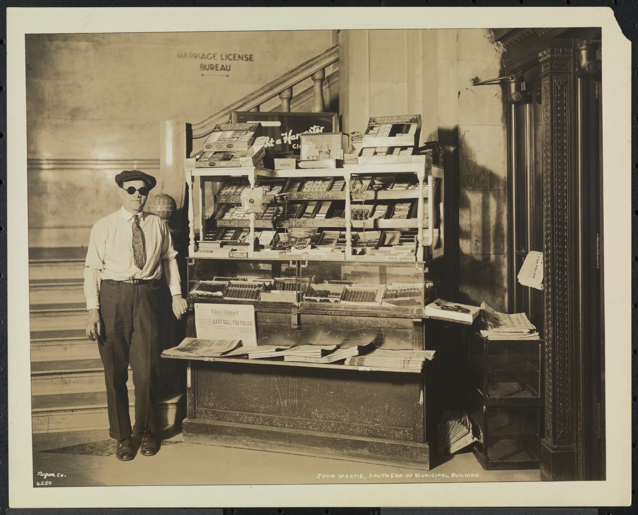 Blind news dealer, John Martie, at his stand at the south end of the Municipal Building, New York by Company Byron
