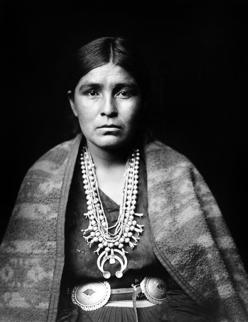Navajo woman wearing silver squash blossom necklace, concho belt, blanket draped over shoulders, photo Edward S. Curtis by Edward Sheriff Curtis