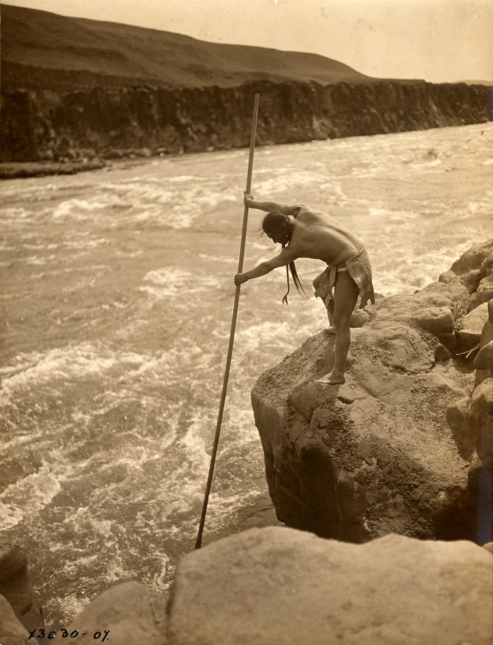 Tlakluit Indian, standing on rock, fishing with dip net by Edward Sheriff Curtis