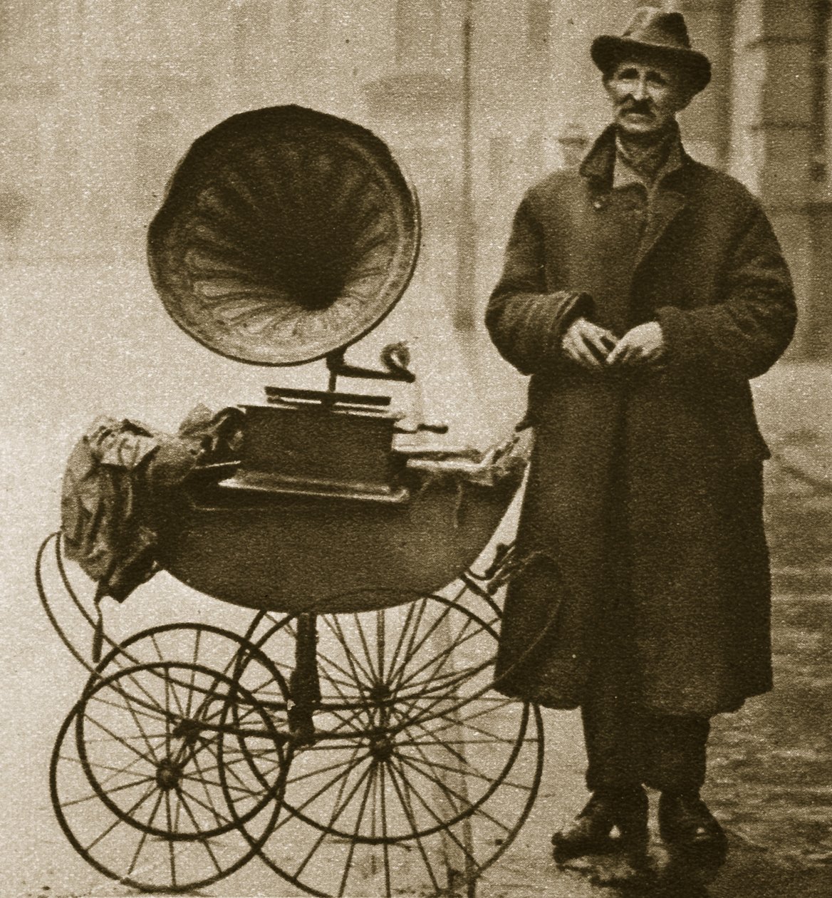 A street hawker entertains with a gramophone, transported in a pram by English Photographer