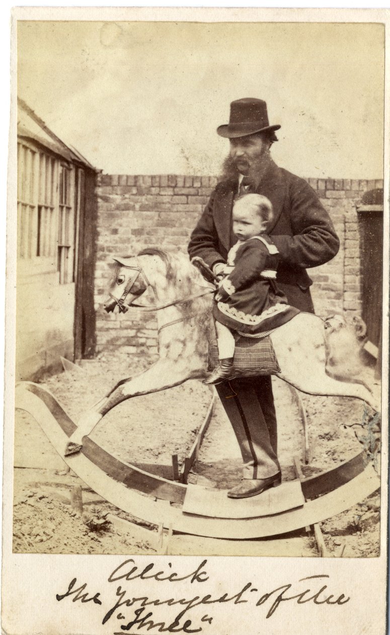 Young girl on a rocking horse in the garden, her father beside by English Photographer