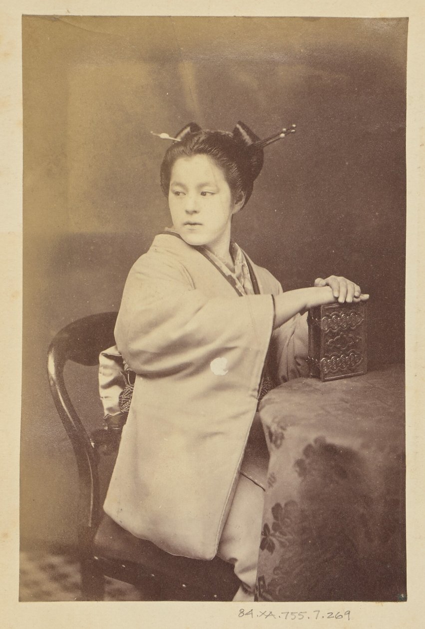 Seated Japanese woman holding a cartes-de-visite album at a table by Felice Beato