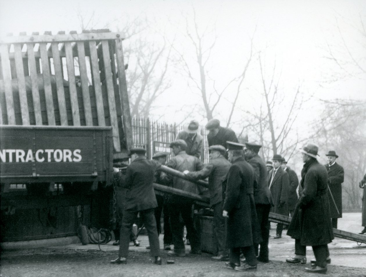 A crowd of onlookers stand by as a Rhinoceros is unloaded from a truck, by keepers, at London Zoo in 1924 by Frederick William Bond