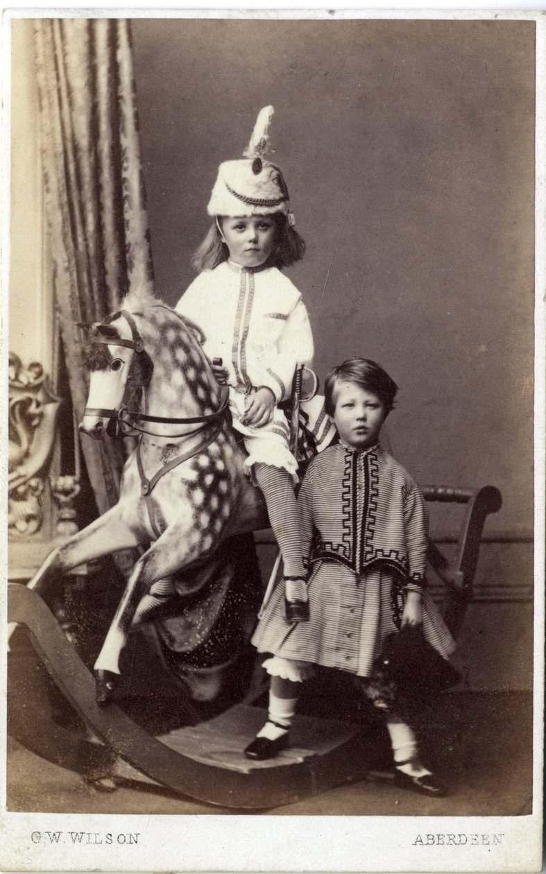 Young girl with hat on rocking horse with another girl standing by by George Washington Wilson