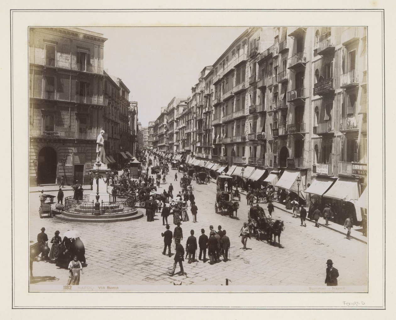 View of Via Roma in Naples with a Statue, Shops, Horse Carriages, and Passersby by Giorgio Sommer