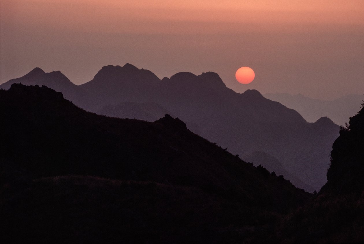 Brilliant crimson, orange sun sets over the Yan Shan Range by James L Stanfield