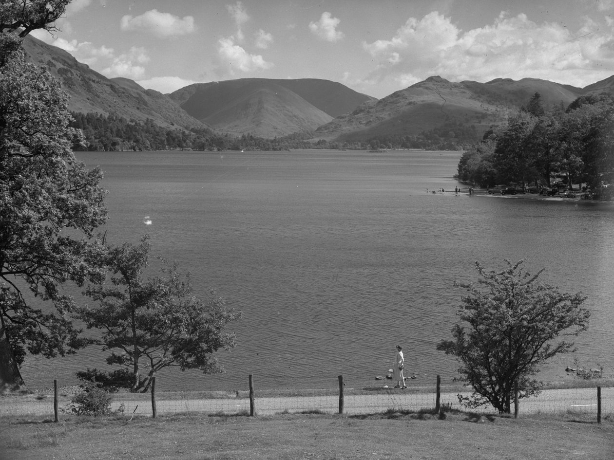 A lady looking across a lake, cars parked with people playing in the water, hills in background by Joseph Hardman
