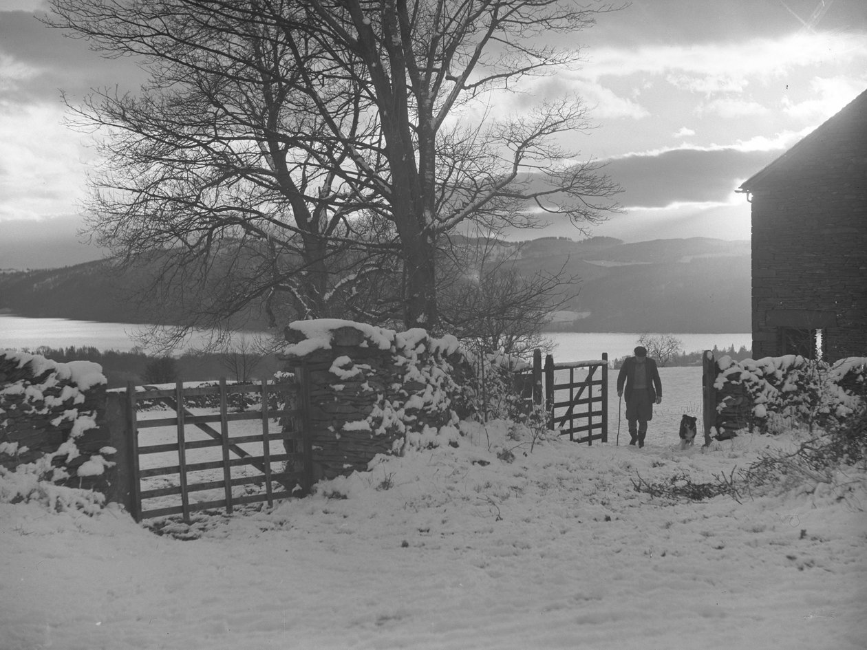 Man and dog walking through gate towards camera in snow with Thirlmere behind by Joseph Hardman