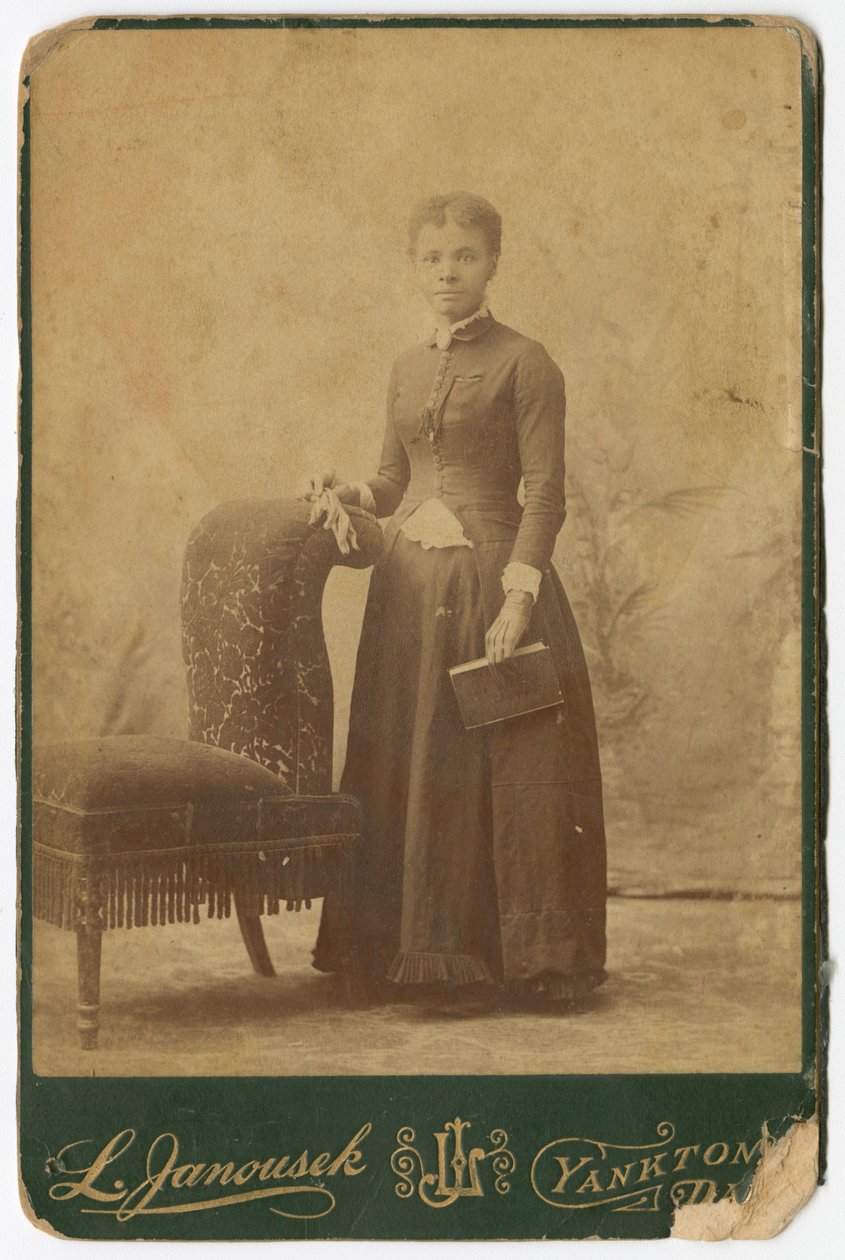 Photograph of a woman standing next to a chair and holding a book by Louis Janousek