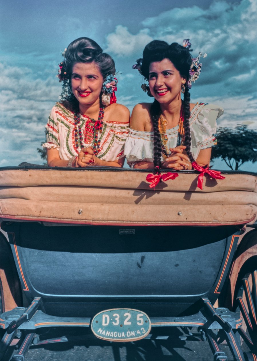 Young Nicaraguan women pose in festive costumes and headgear in back of a carriage by Luis Marden