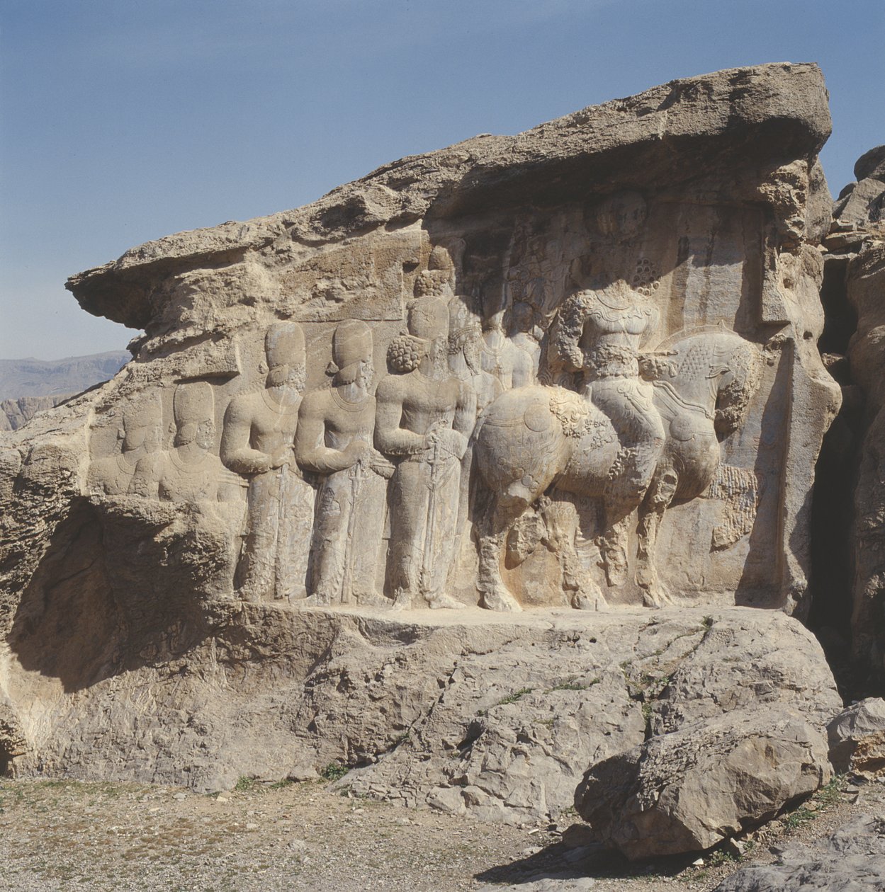 Rock relief depicting Shapur I and his family wearing heraldic emblems on their hats, with a tri-lingual inscription on the horse in Greek, Parthian and Middle Persian by Sasanian