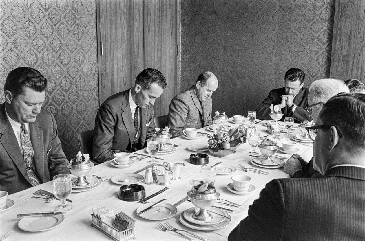 Businessmen praying before beginning to eat lunch at a church fundraising meeting by Ted Spiegel