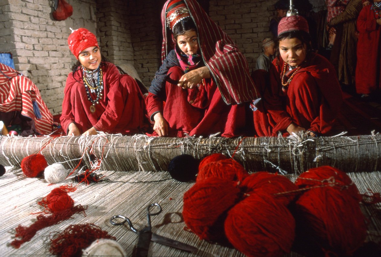 Turkoman tribeswomen weavers trim knots in the warp of a rug on a loom in a village by Thomas J. Abercrombie