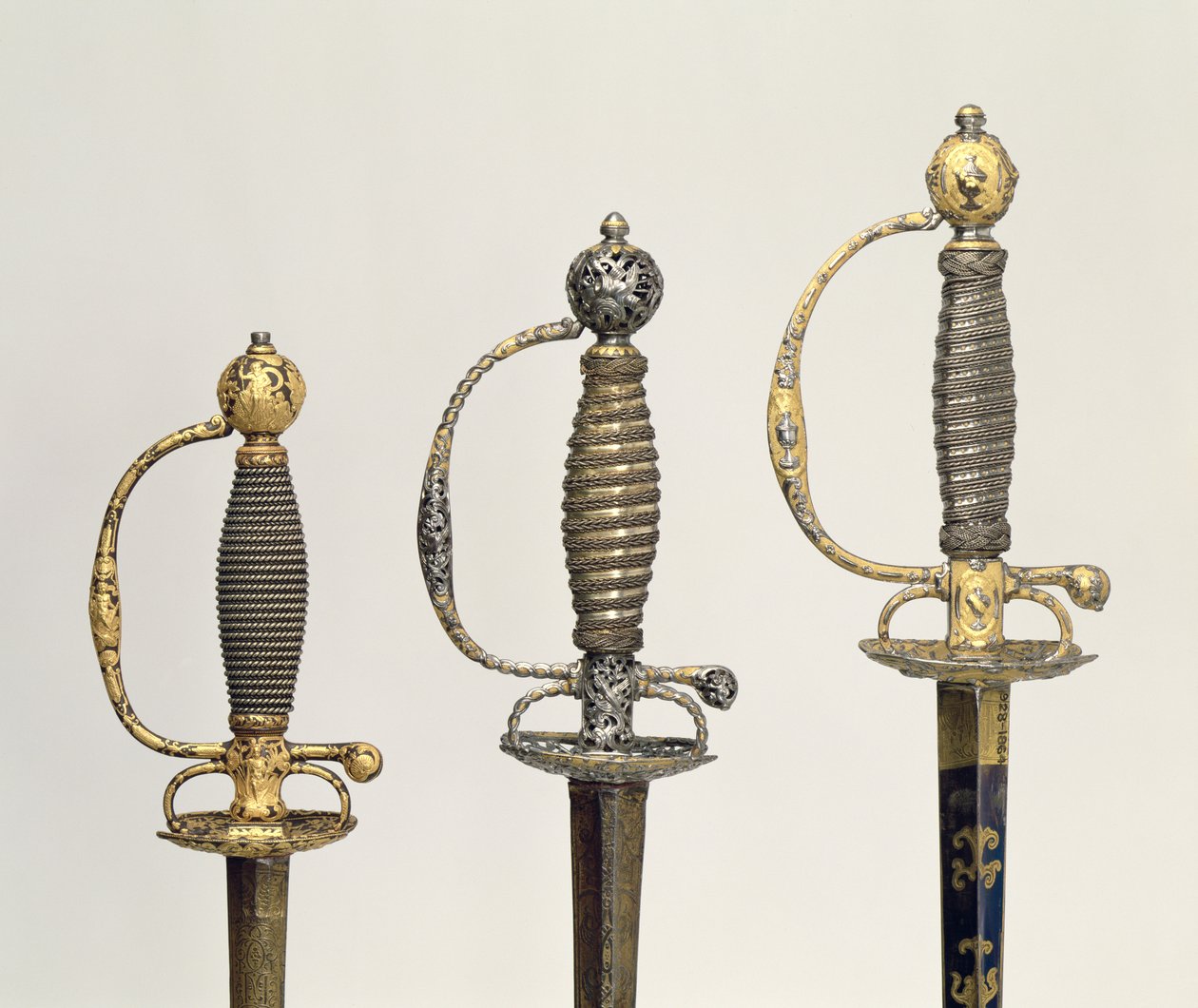 Hilts of three French swords: one of steel, blued and overlaid with designs in chased gold, c.1730; one of steel pierced and chiselled and the ground of matted gold, c.1760; one of chiselled steel by Unbekannt Unbekannt