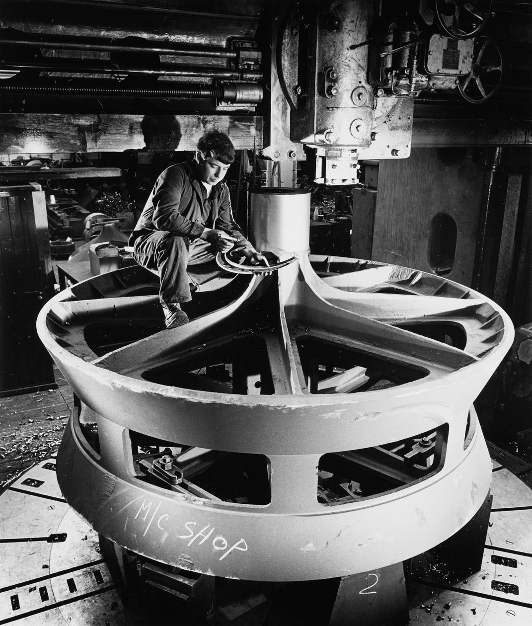 A fitter on top of a large cast item uses vertical boring machine by Unbekannt