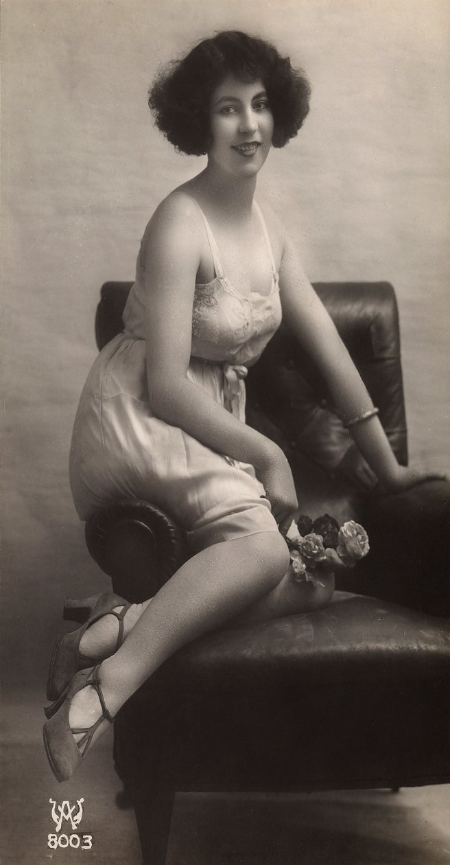 A young woman posing in her petticoat, sitting in an armchair by Unknown photographer