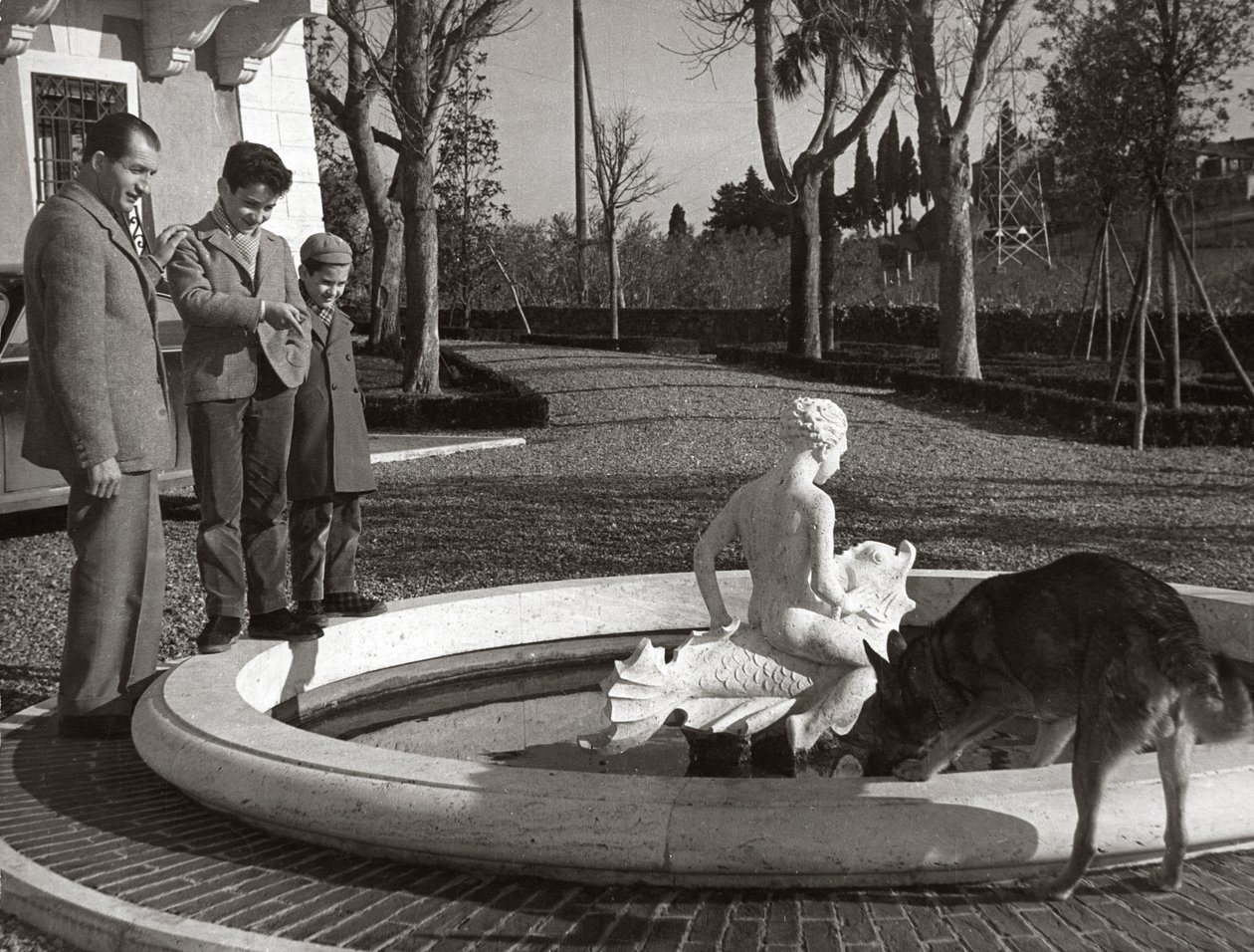 Gino Bartali with two kids and a dog near a fountain by Unknown photographer