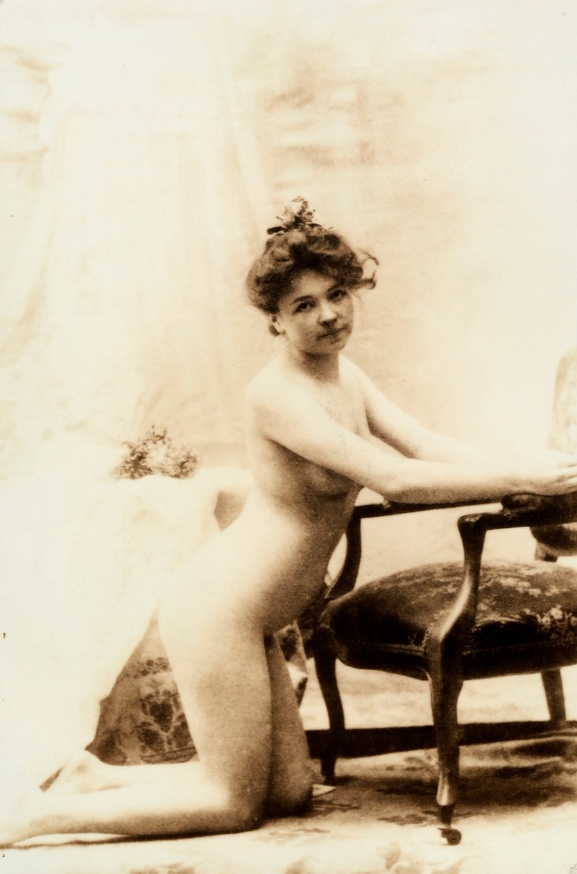 Nude portrait of a young woman kneeling in front of a small armchair by Unknown photographer