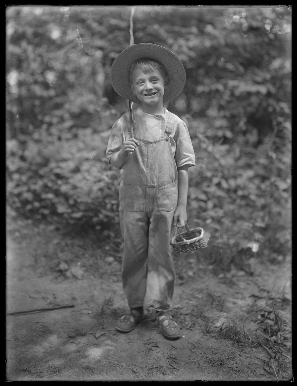 William Gray Hassler in straw hat and overalls, carrying fishing pole and basket in the woods by William Davis Hassler