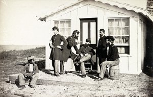 Five Civil War soldiers gathered on dirt porch outside home, African American youth seated near them