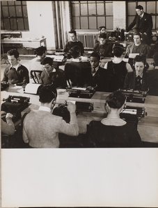 People sit in front of typewriters while wearing headphones