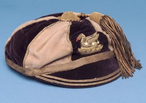 Blue and white segmented football cap with metal dragon badge and gold tassel by English School