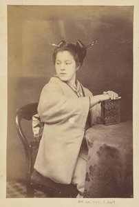 Seated Japanese woman holding a cartes-de-visite album at a table by Felice Beato