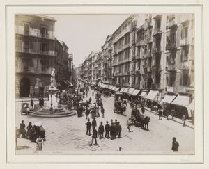 View of Via Roma in Naples with a Statue, Shops, Horse Carriages, and Passersby