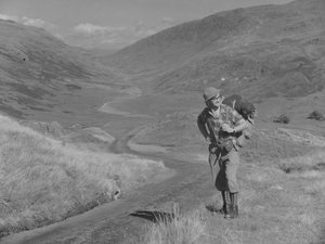 A man walking with a rucksack on his back in an open valley landscape by Joseph Hardman