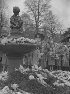 Children placing bunches of daffodils on fountain with statue on top by Joseph Hardman