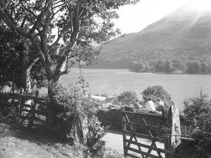 Four people having a picnic on a dry stone wall overlooking a lake, car parked with boot open by Joseph Hardman