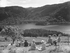 Group of people sitting on grass or deck chairs looking at a view of Thirlmere by Joseph Hardman