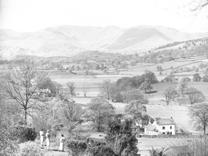 Three women standing looking out across a lake at Esthwaite, hills in the background