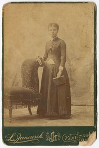 Photograph of a woman standing next to a chair and holding a book