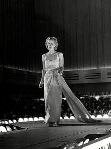 Model photographed on a runway in evening dress with rhinestone shoulder straps; the article is a creation of the couture house 