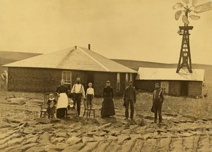 Family of Homesteaders, Outside of Their Sod House with a Windmill on the Roof of the Adjoining Building in Custer County, Nebraska by Solomon D. Butcher