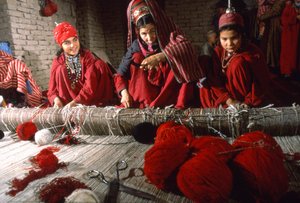 Turkoman tribeswomen weavers trim knots in the warp of a rug on a loom in a village