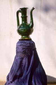 Woman in Kabul secluded from view by silk chadri carries jug